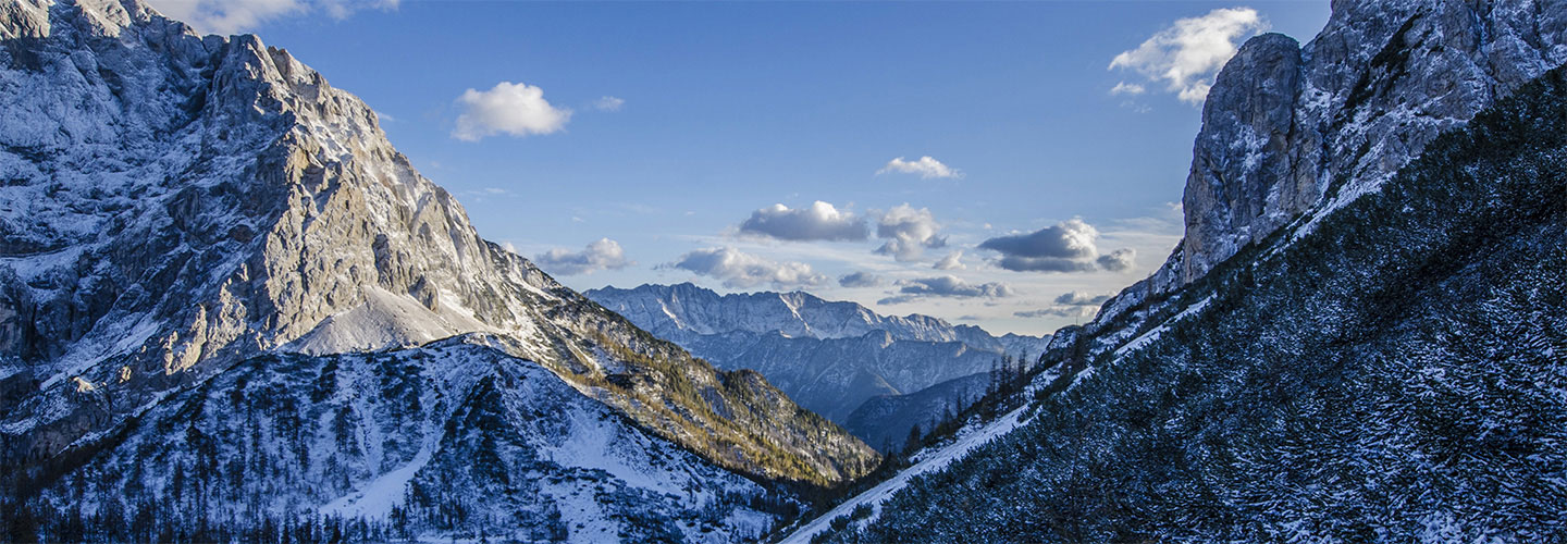 Vallée de montagne enneigée entre deux sommets rocheux, sous un ciel bleu